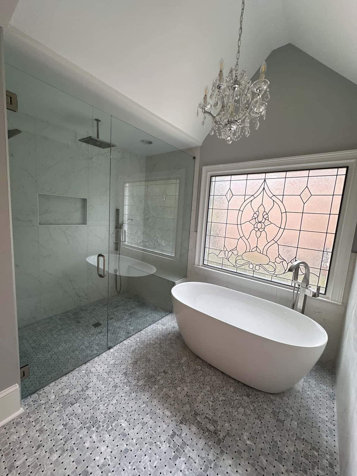 Glass-enclosed wet room with a freestanding tub, crystal chandelier, leaded glass window and basketweave marble floor