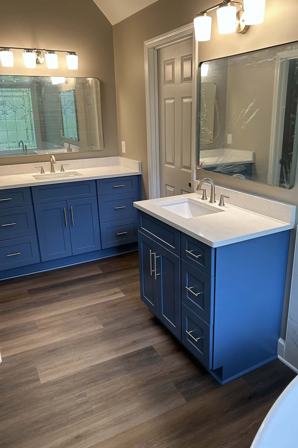 Two cobalt blue shaker vanities with white quartz tops, framed mirrors and chrome fixtures on wide-plank flooring