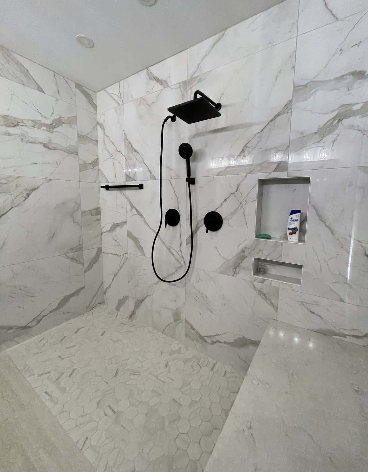 Curbless marble-look tile shower with a matte black rain head, handheld shower and built-in niches