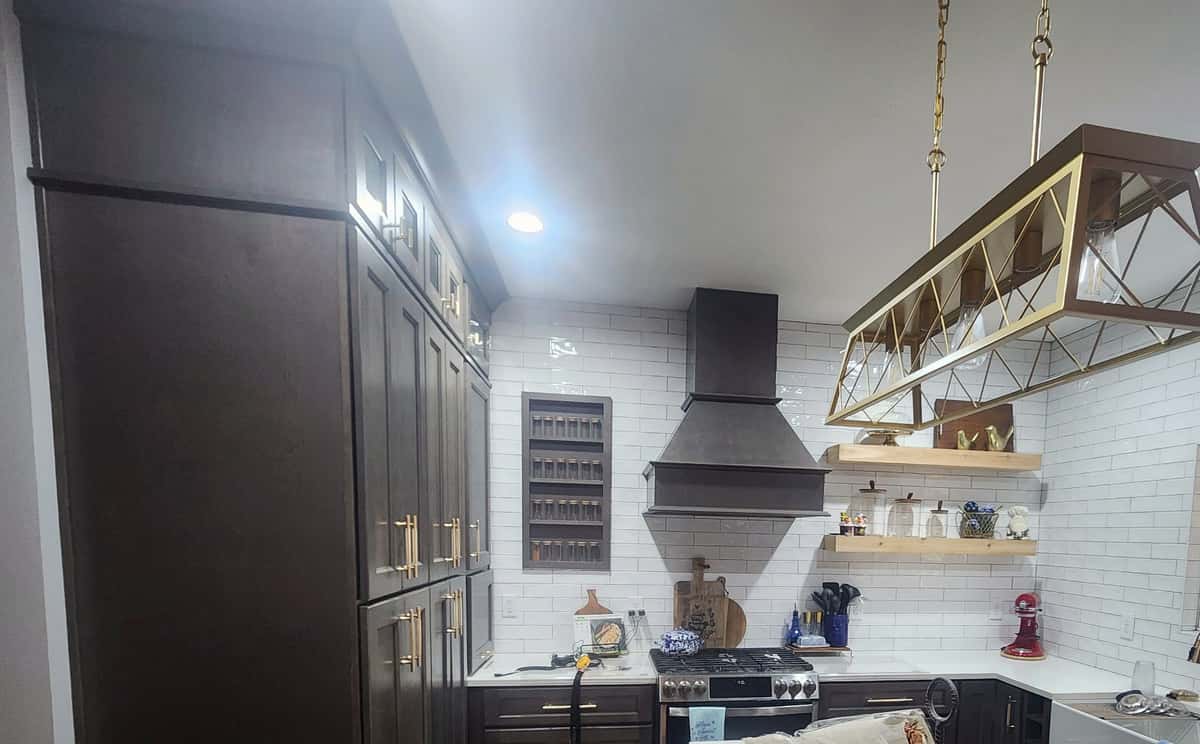 Espresso shaker kitchen with a brass lantern pendant, wood range hood, recessed spice niche, floating oak shelves and white quartz island