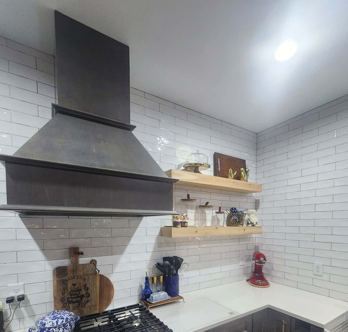 Custom wood range hood over a gas range with floating oak shelves, glossy white subway tile and espresso cabinets with brass pulls