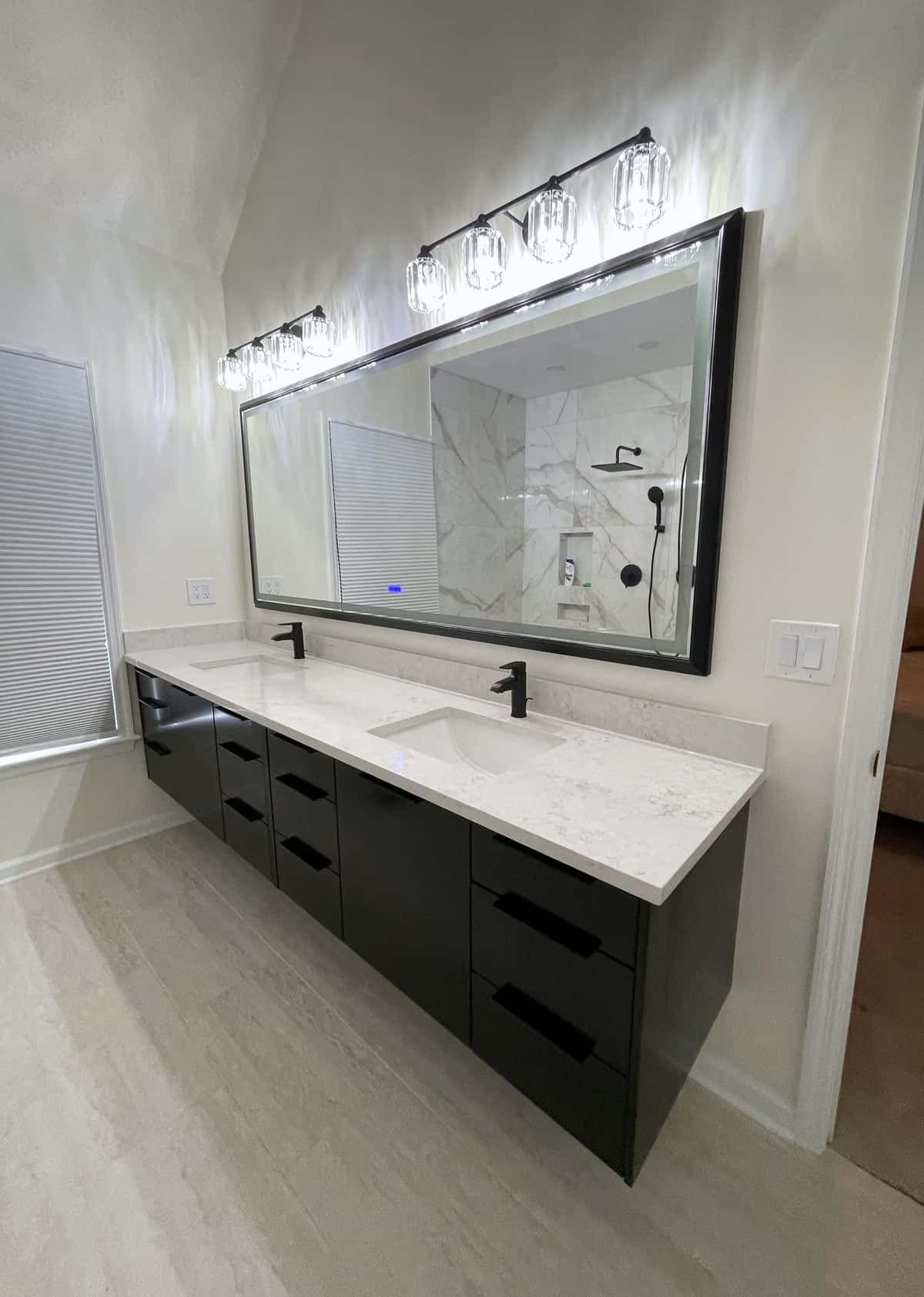 Floating black double vanity with a white quartz top, framed black mirror and crystal vanity lights