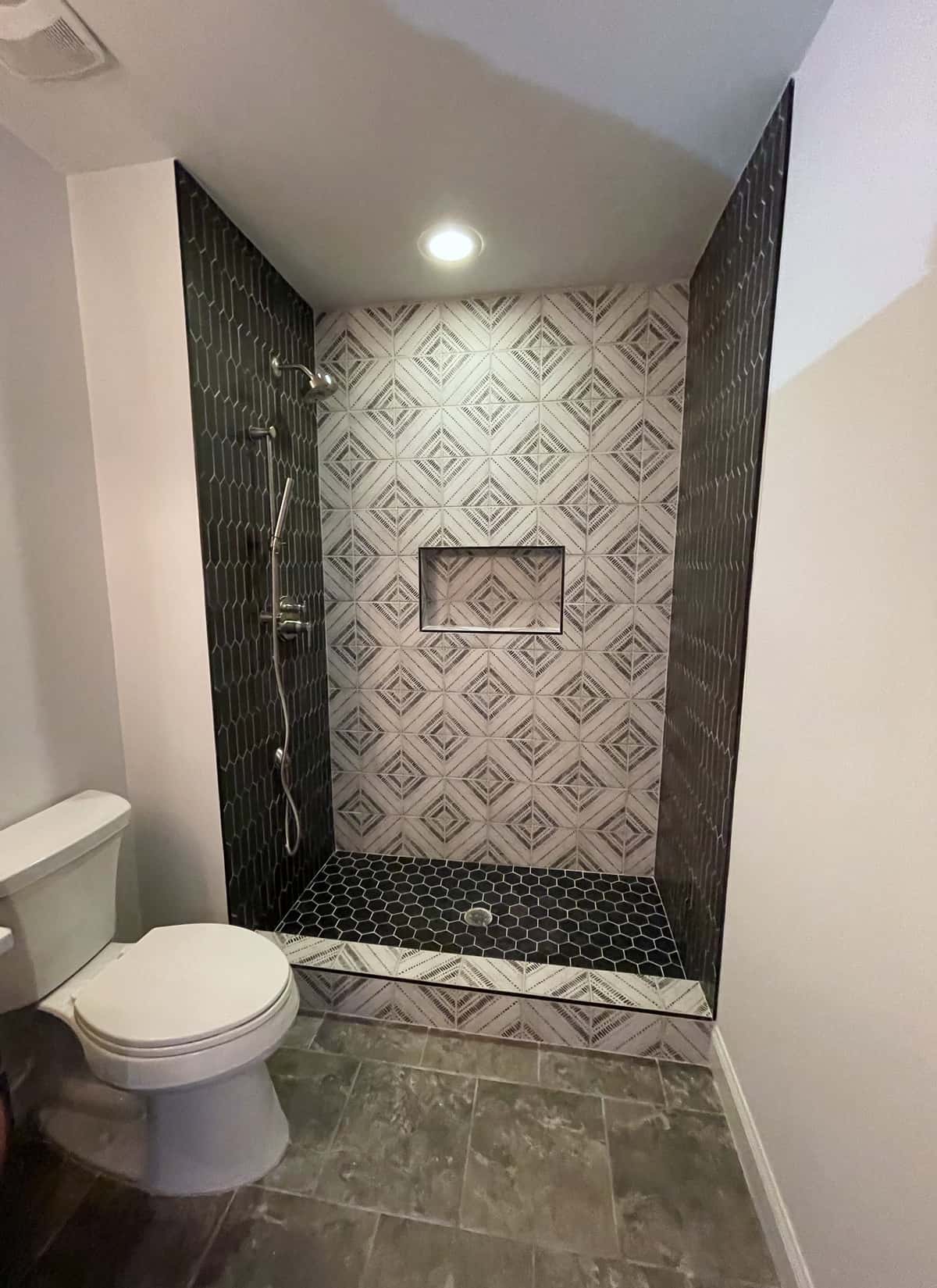 Walk-in shower with a geometric patterned tile feature wall, black tile side walls, recessed niche and hex mosaic floor