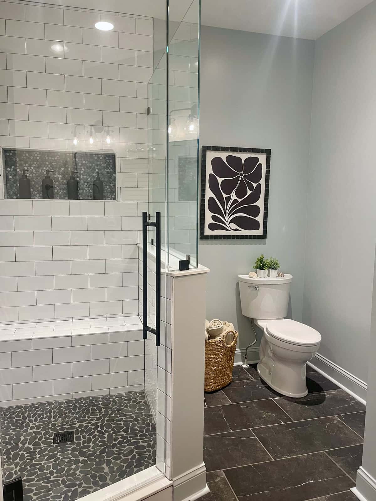 Frameless glass shower with white subway tile walls, a black pebble mosaic floor and niche, and matte black hardware