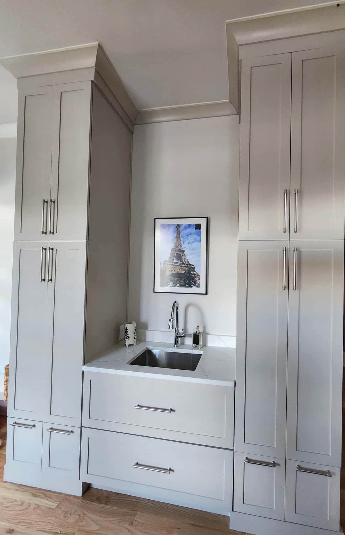 Floor-to-ceiling greige shaker built-ins with crown molding flanking a quartz-topped prep sink station