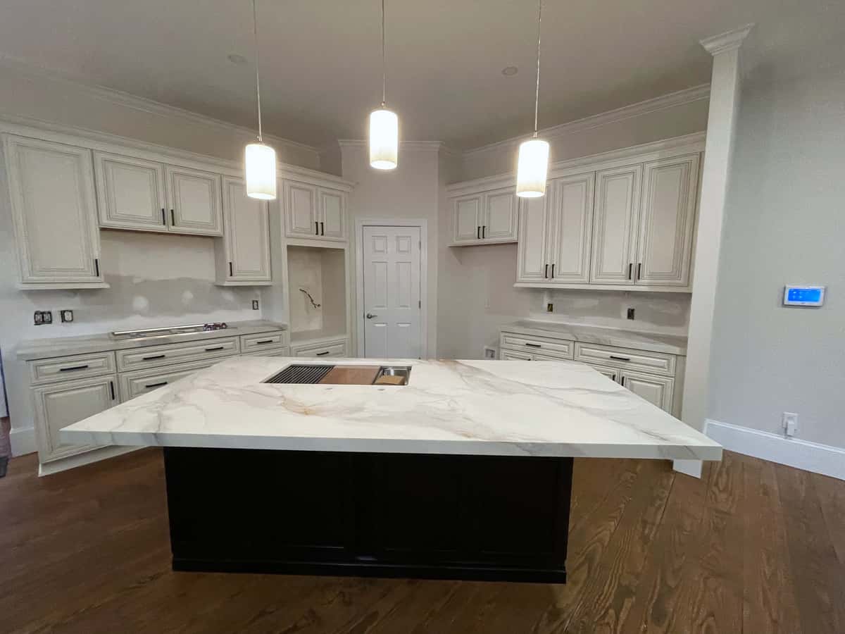 Ebony kitchen island with a waterfall-edge marble-look top under three glass pendants, surrounded by white cabinetry