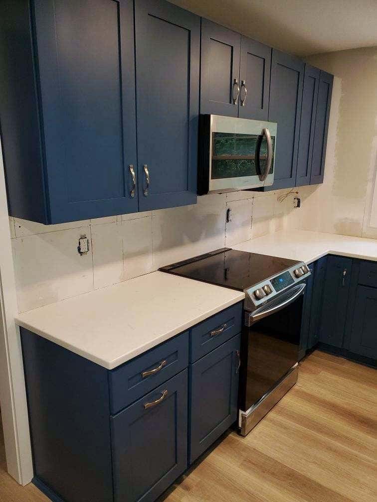 Navy shaker kitchen mid-install with quartz countertops set, before the tile backsplash