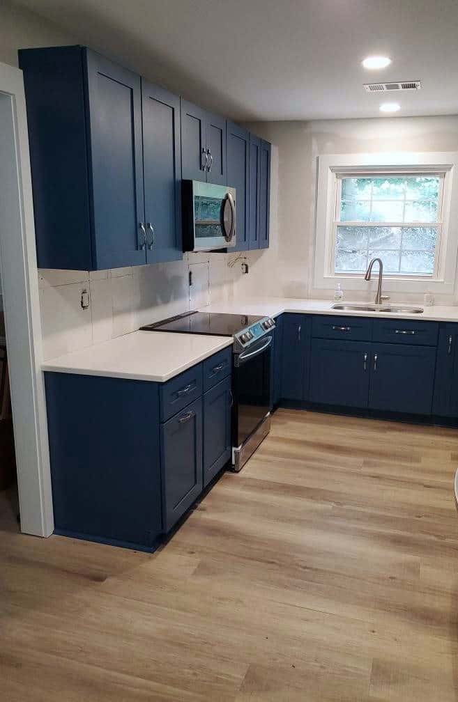 Navy shaker kitchen with white quartz countertops, window sink run and light oak-look flooring
