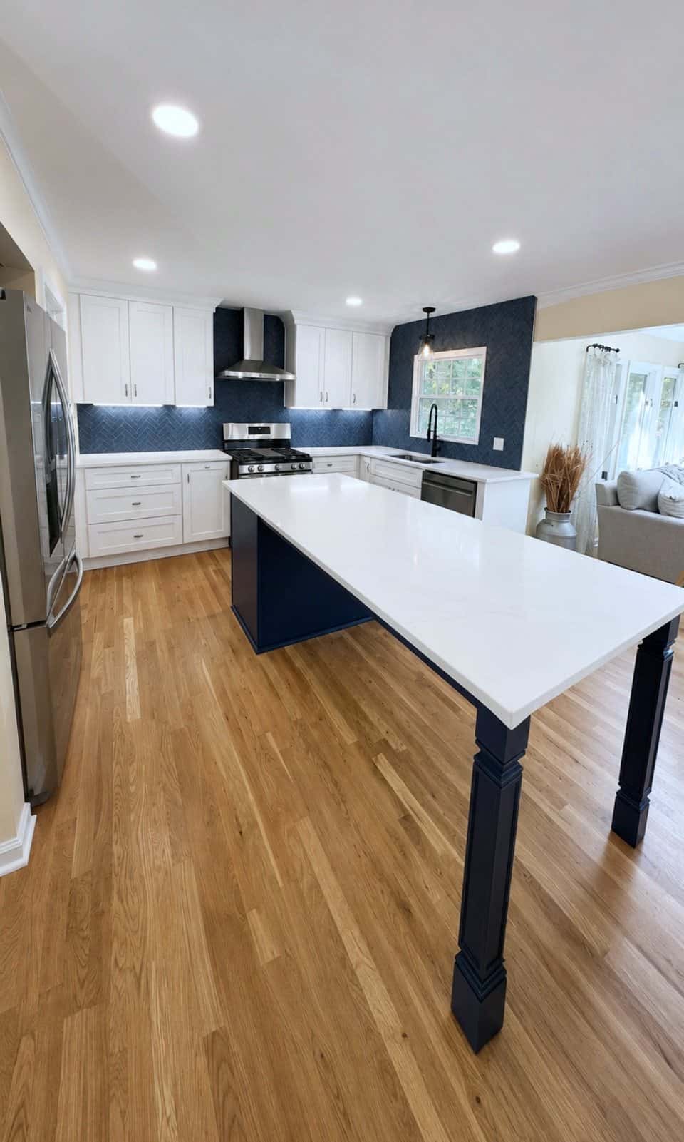 Open-plan white kitchen with a navy peninsula, white quartz countertops, navy tile backsplash and refinished oak floors