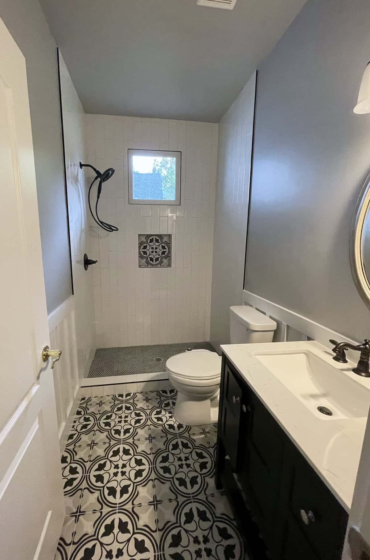 Hall bath with black and white patterned floor tile, white wainscoting, a black vanity and a white tiled walk-in shower