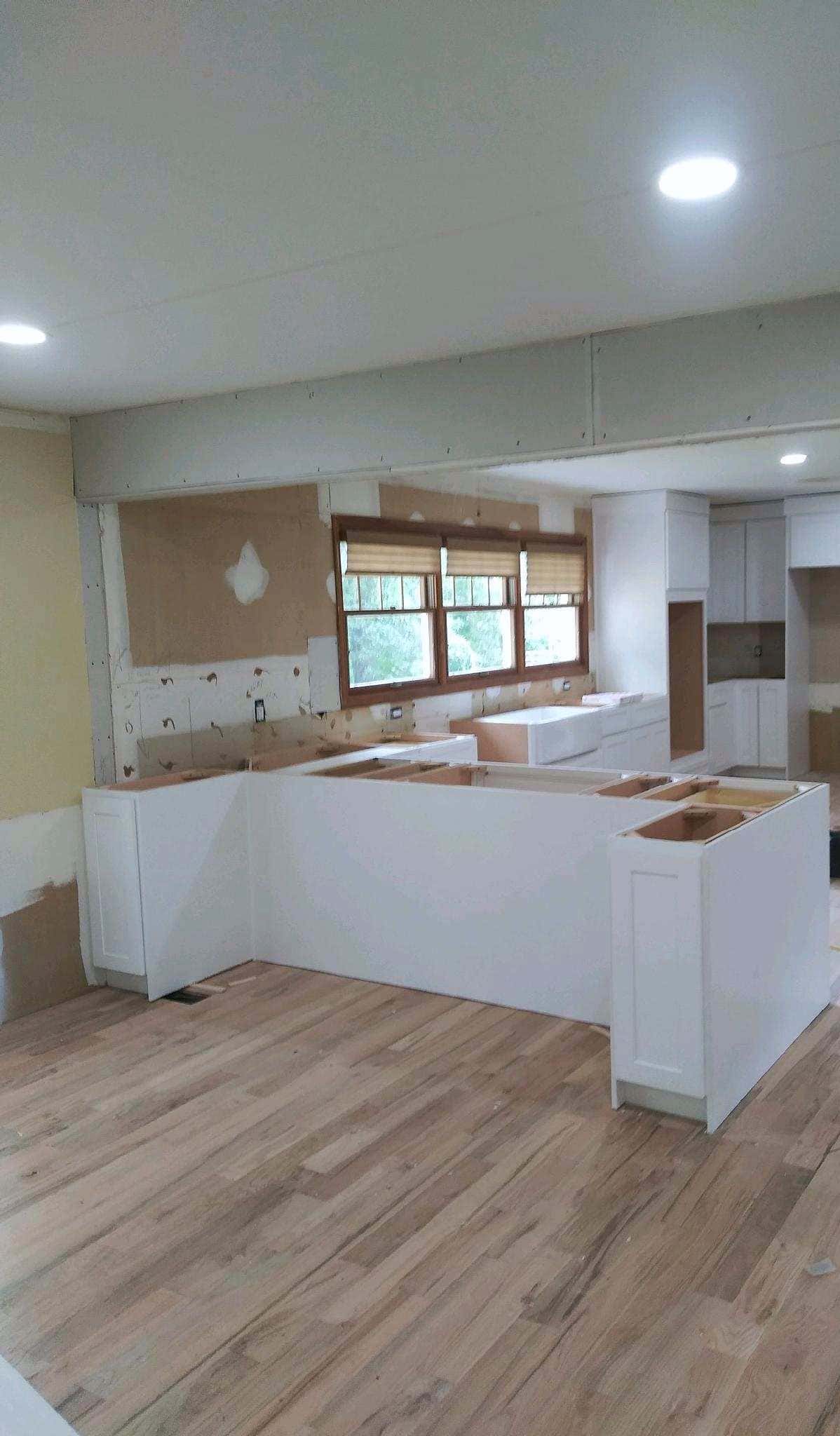Open-plan white kitchen during cabinet installation on refinished oak floors, before countertops