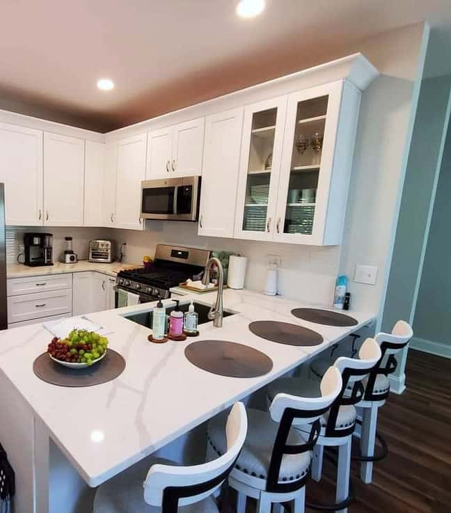 Bright white shaker kitchen with a veined quartz peninsula, glass-front upper cabinets and counter seating