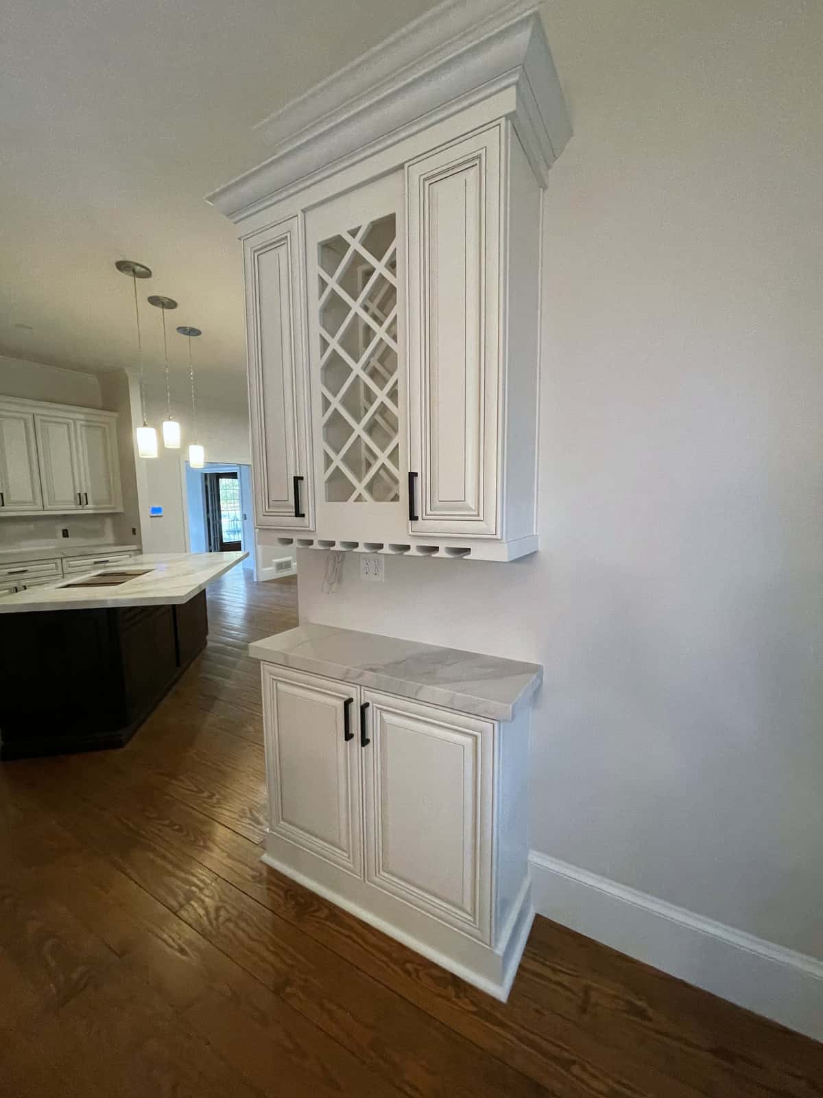 White raised-panel hutch with a wine lattice and crown molding, open to a kitchen with an ebony island and pendant lights