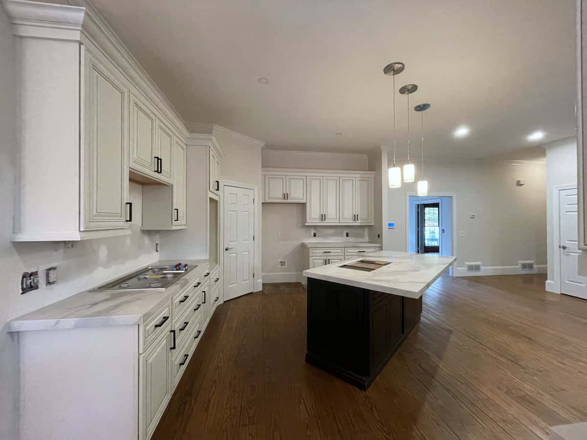 Long white raised-panel kitchen with stacked upper cabinets, an ebony island with a marble-look top and oak floors