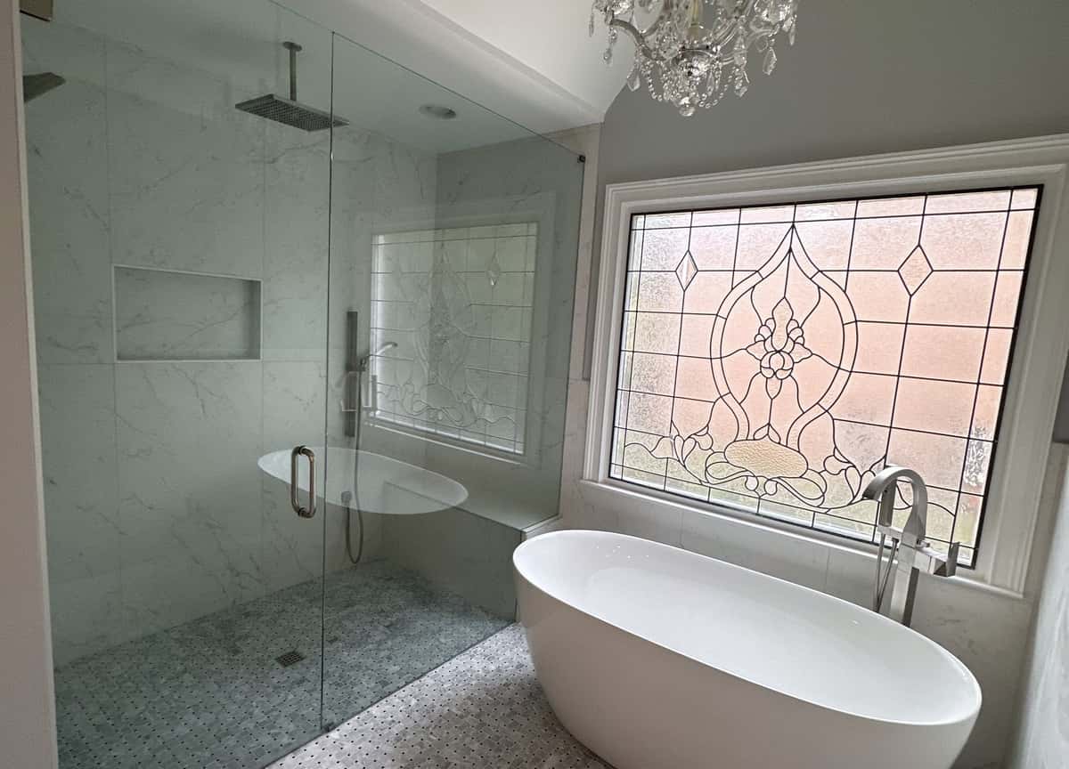 Primary bath with a crystal chandelier, leaded glass window, freestanding tub and glass-enclosed wet room